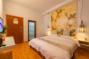 Een slaapkamer met een groot bed, houten vloeren, een bureau met een computer, een deur met een WiFi-bordje en een muur met een bloemschilderij.