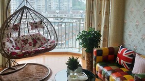 A living room with a hanging chair, a colorful sofa, a small table with a vase, and a potted plant.