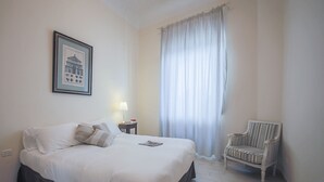 Ein Hotelzimmer mit einem Bett, einem Sessel, einem Nachttisch, einer Lampe und einem Fenster mit Vorhängen.