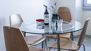 Ein runder Glastisch mit vier Holzstühlen, einer Weinflasche, einem Krug mit Blumen und einem roten dekorativen Gegenstand.
