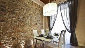 A dining area with a stone wall, a table set for four, white chairs, and a hanging light fixture. - Giglio Santa Trinita (Florence)