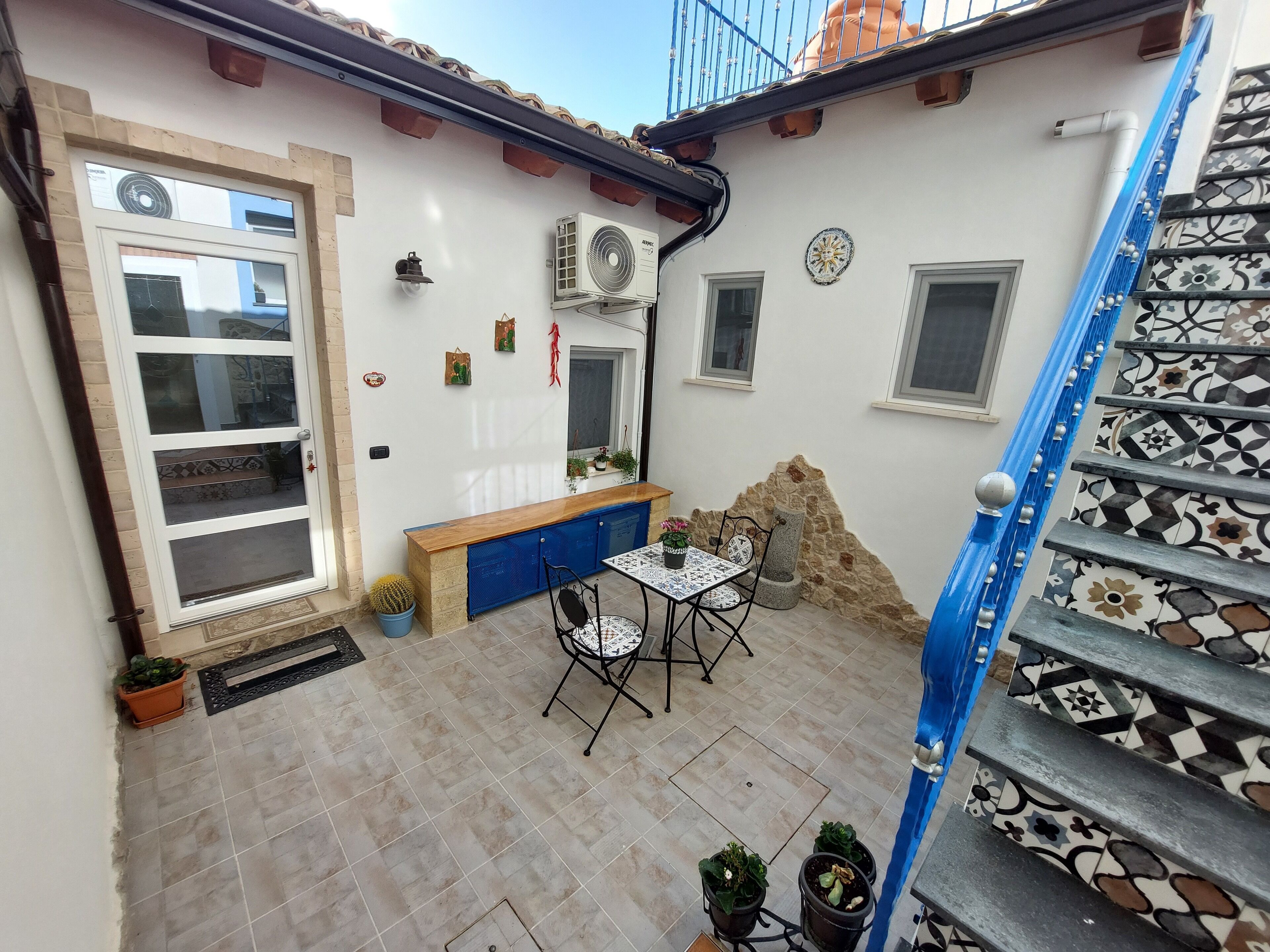 A courtyard with a tiled floor, a blue staircase, a small table with chairs, and a blue cabinet.