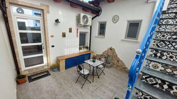 A courtyard with a tiled floor, a blue staircase, a small table with chairs, and a blue cabinet.