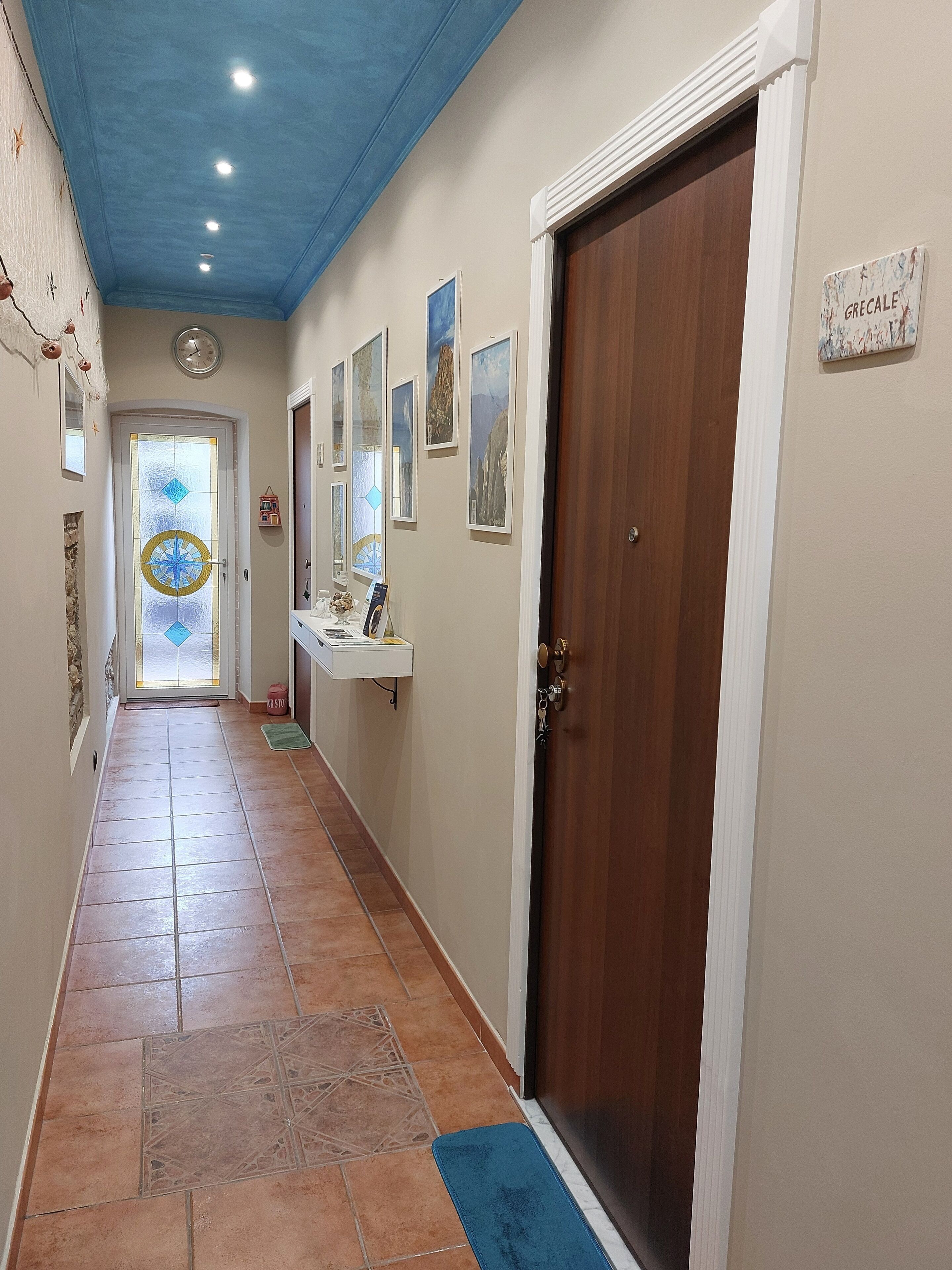 Un pasillo con suelo de baldosas, una puerta de madera y un muro decorado con cuadros.