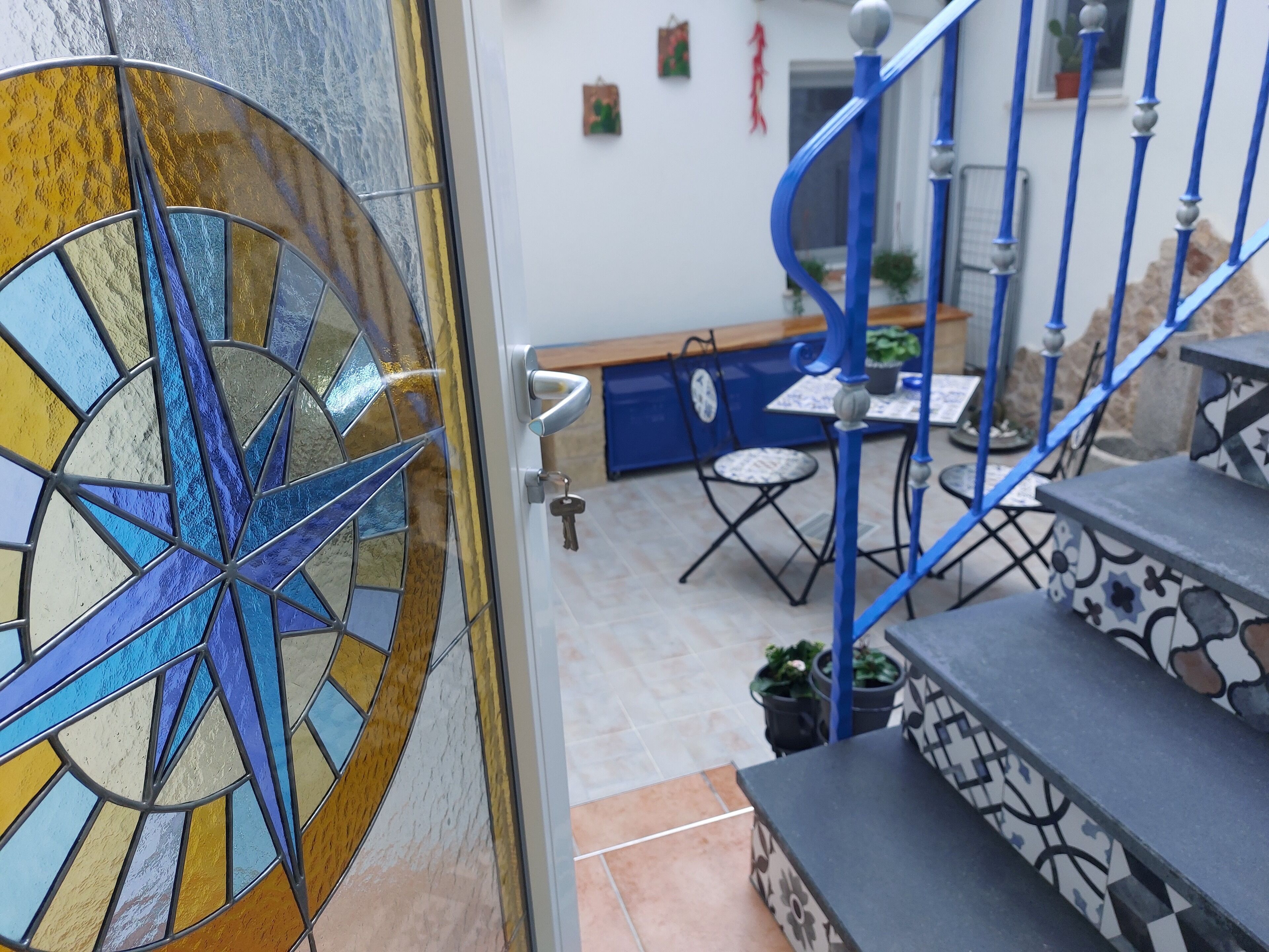 Eine Buntglas-Tür mit Sternenmuster, eine blaue Wendeltreppe und eine kleine Außenbereich-Sitzgelegenheit mit Tisch und Stühlen.