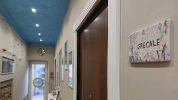 Un pasillo con una puerta identificada con la etiqueta 'GRECALE', un reloj de pared y un adorno mural.