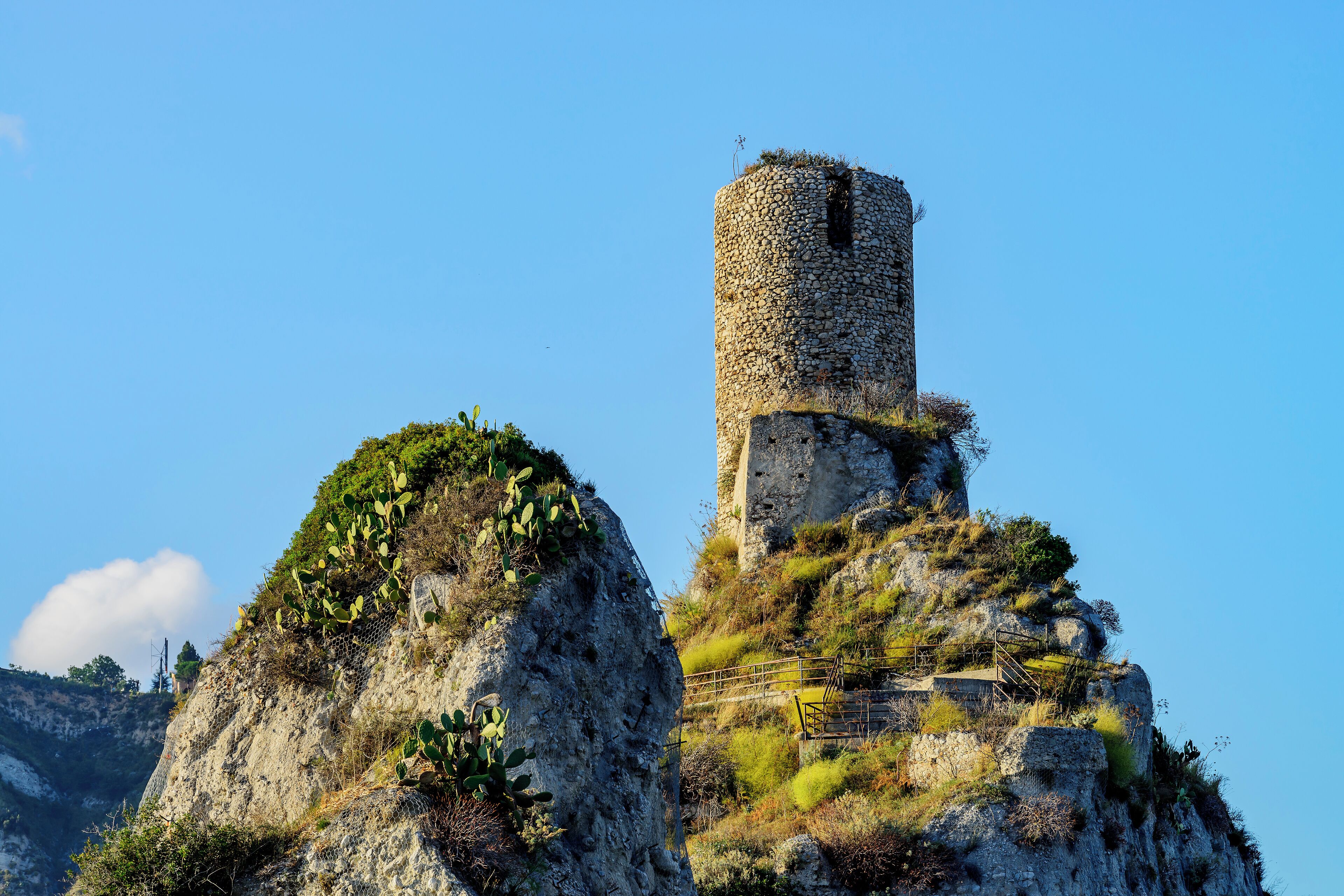Una torre di pietra su una collina rocciosa, con cielo sereno.