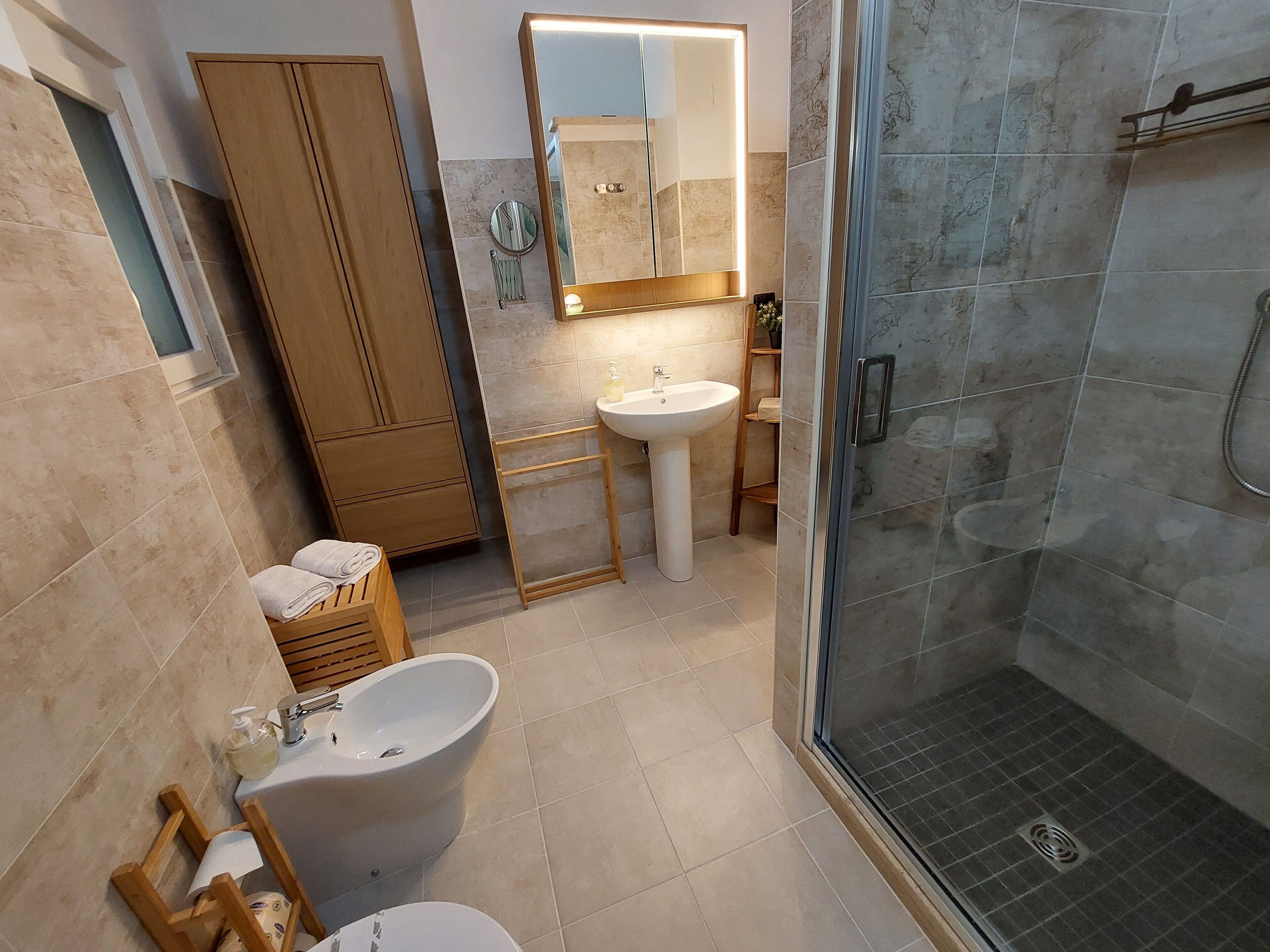 Ein Badezimmer mit Toilette, Bidet, Waschbecken und einer Duschkabine aus Glas.