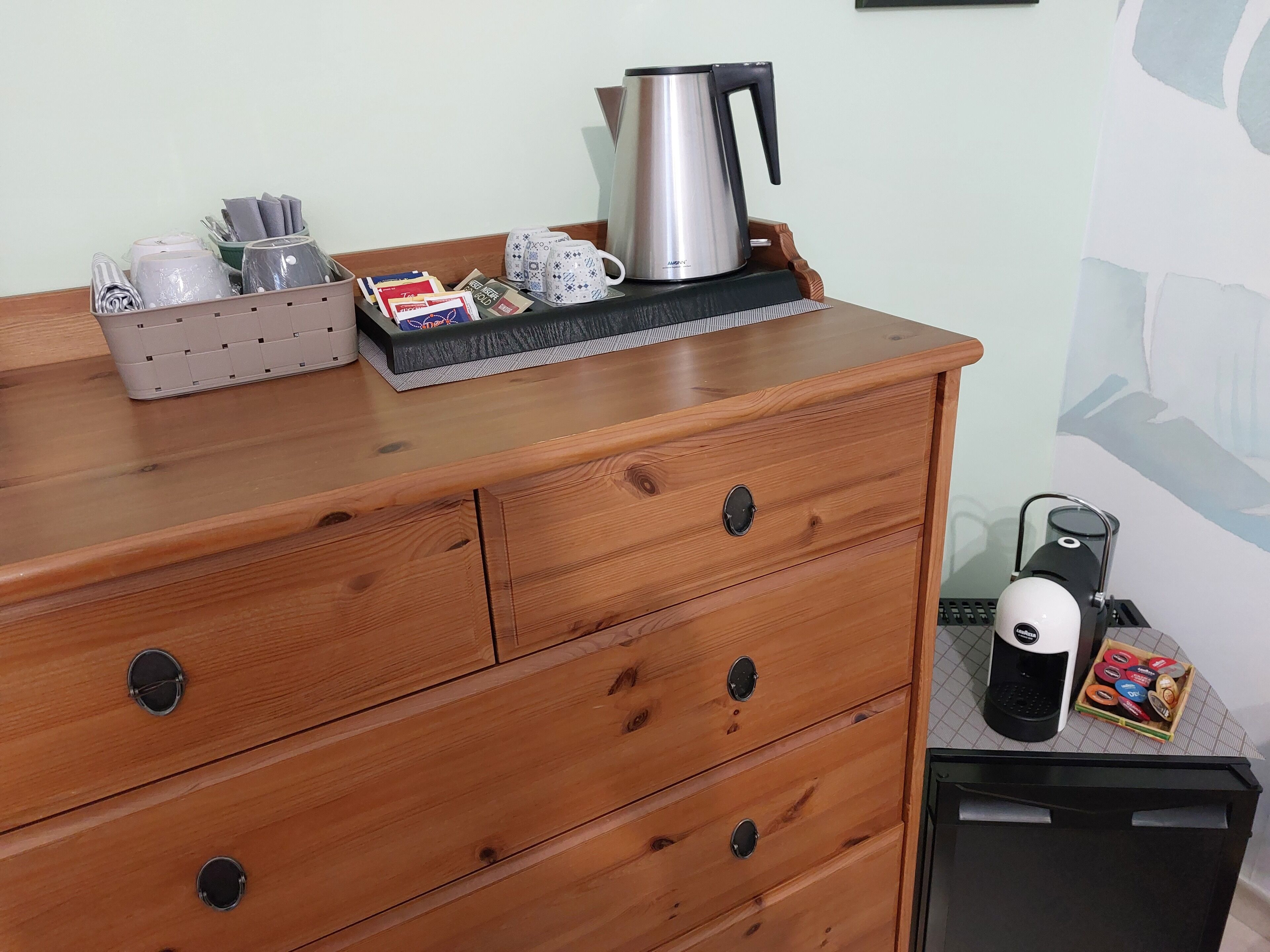 A wooden dresser with drawers, a kettle, a coffee maker, and a box of tea bags.