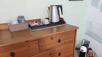 A wooden dresser with drawers, a kettle, a coffee maker, and a box of tea bags.