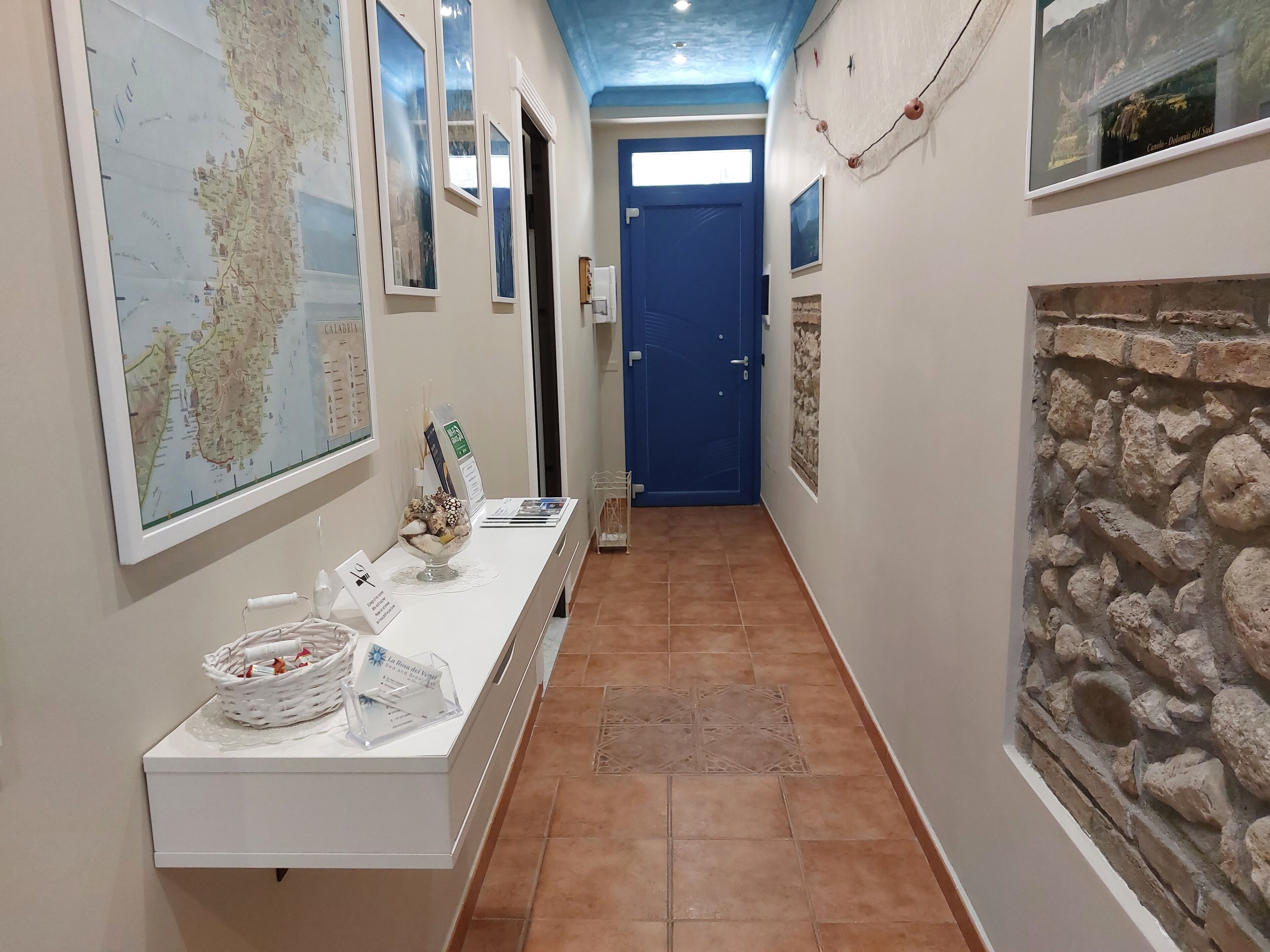 Un couloir avec une carte accrochée sur le mur de gauche, un comptoir d’accueil avec un panier et un panneau, et un mur de pierre sur le côté droit.