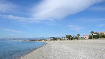 A pebbled beach with a clear blue sky and distant mountains.