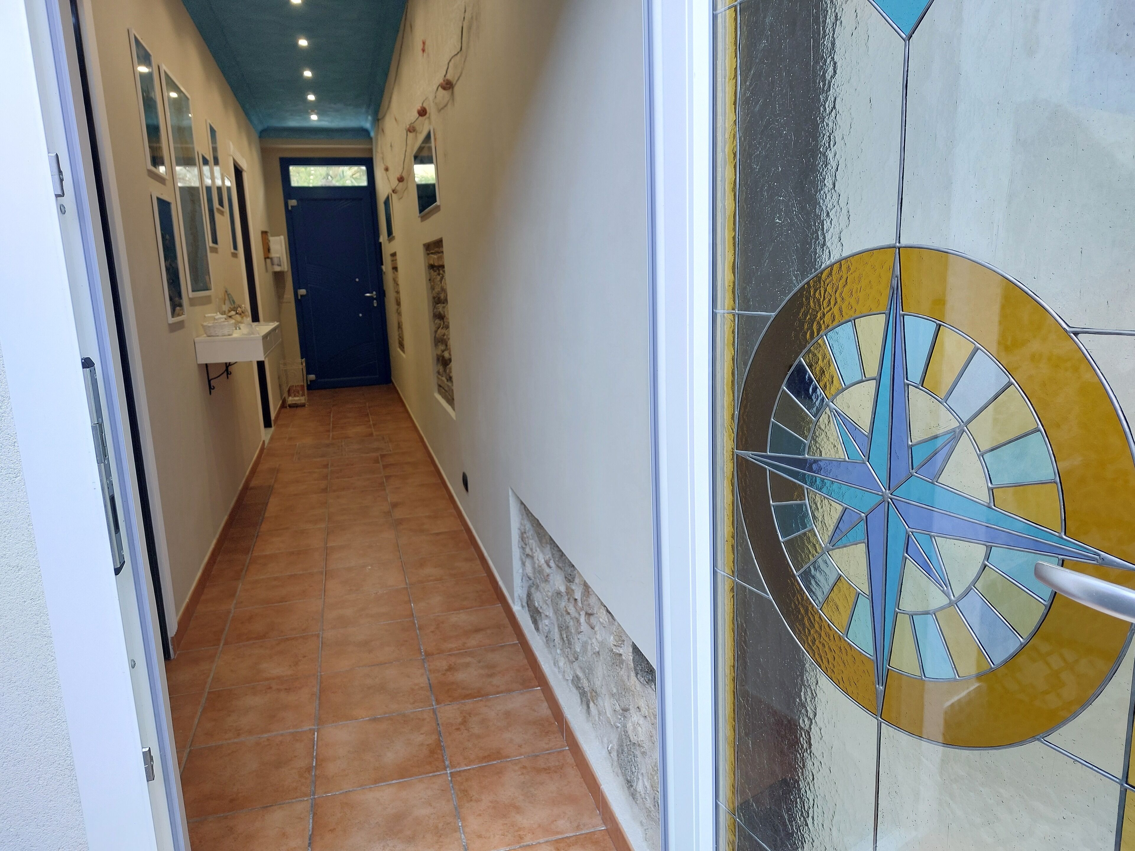 Un couloir au sol carrelé, une porte bleue au fond et une boussole décorative accrochée au mur.