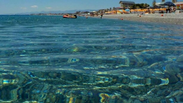 Une plage avec une eau cristalline et un bateau qui se profile à l’horizon.