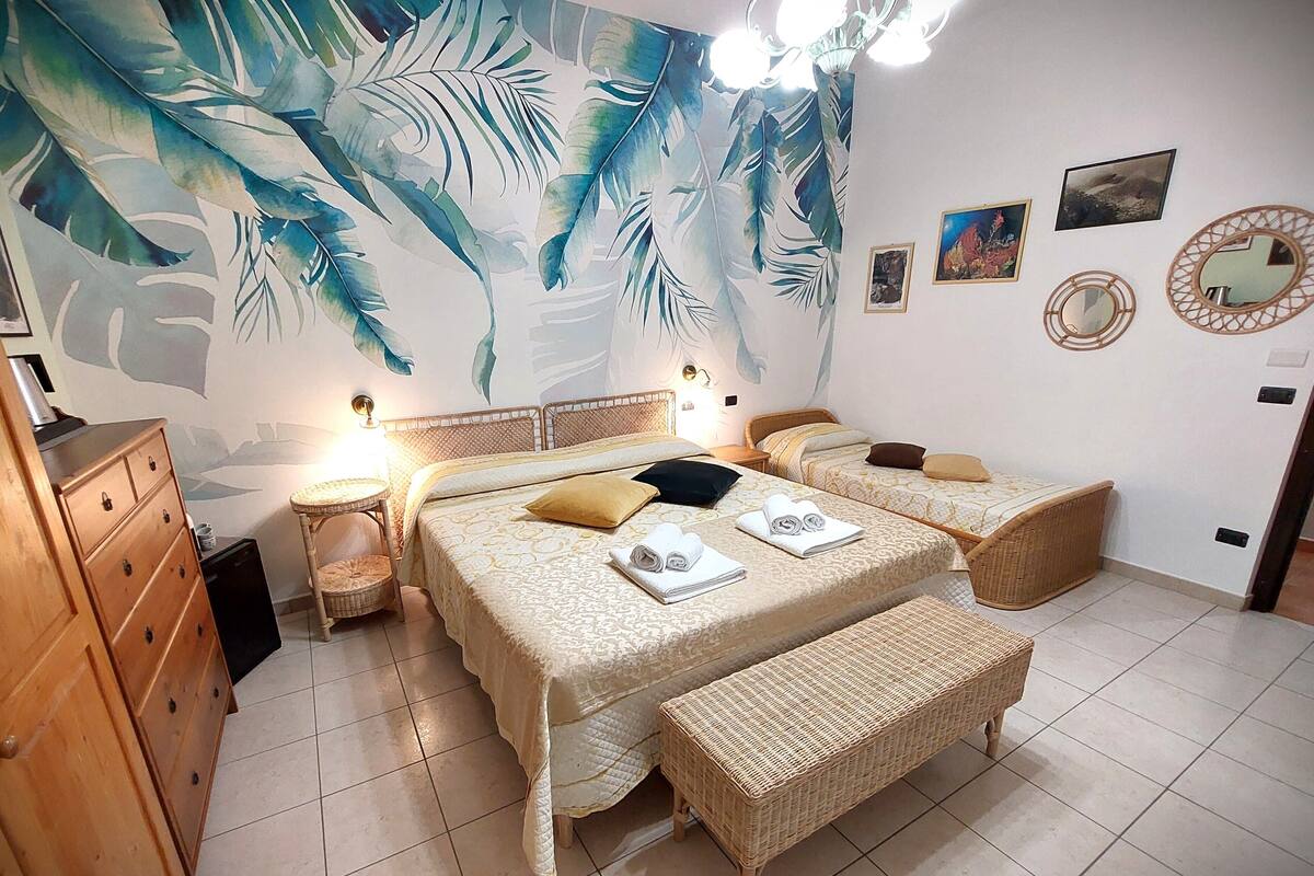 A bedroom with two beds, a wooden dresser, a woven bench, and a wall mural.