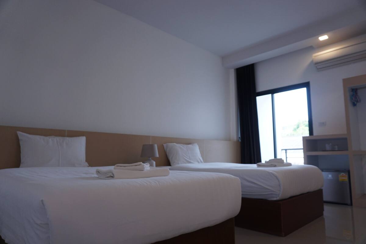 Une chambre d’hôtel avec deux lits, une table de chevet, une lampe et une fenêtre donnant sur un beau paysage.