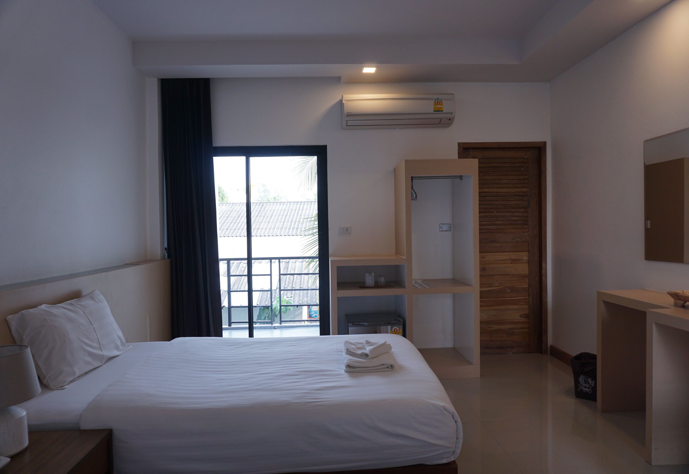 A hotel room with a bed, a desk, a wardrobe, and an air conditioning unit.