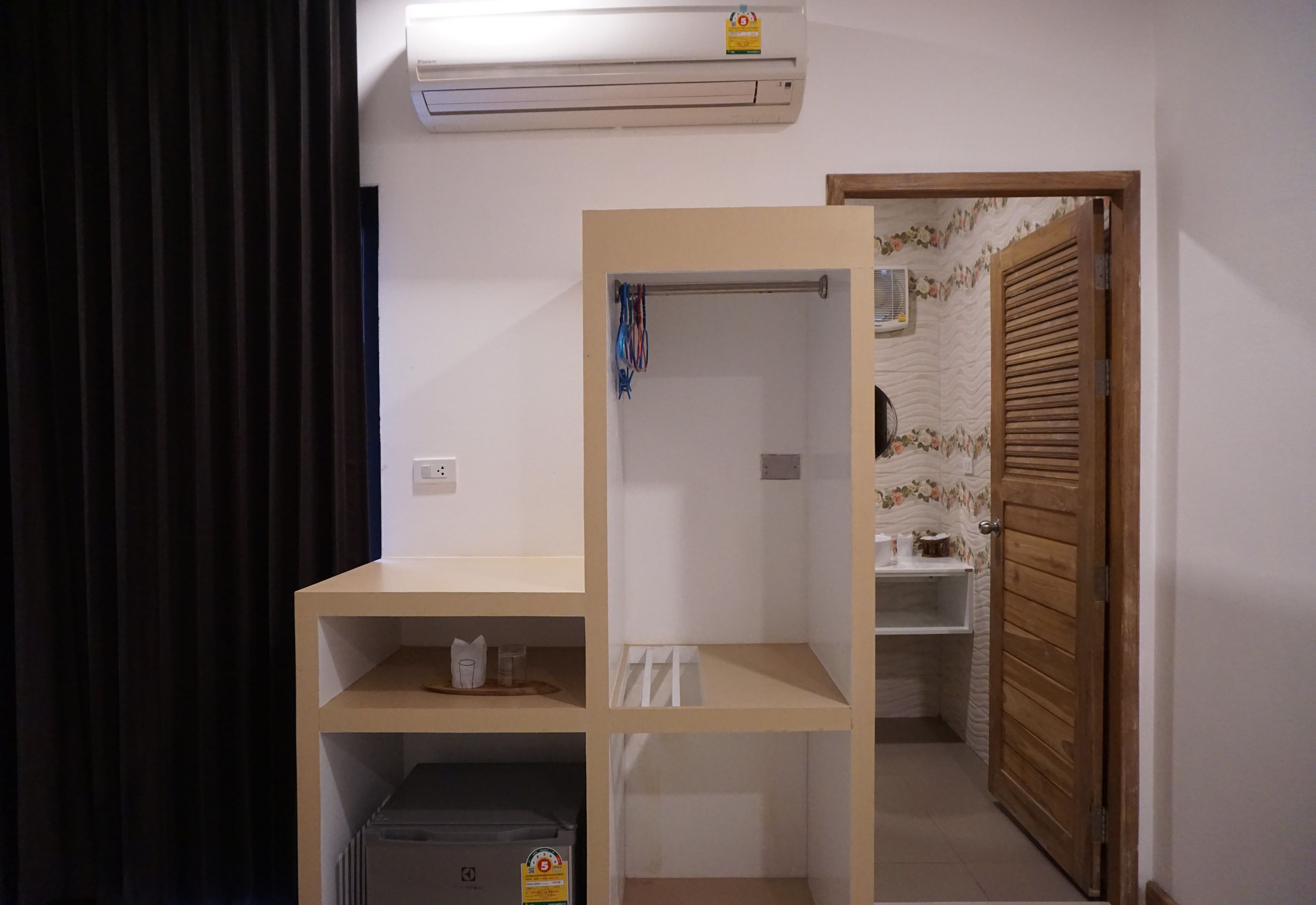 A room with a built-in wardrobe, a small shelf with items, and a door leading to another room.