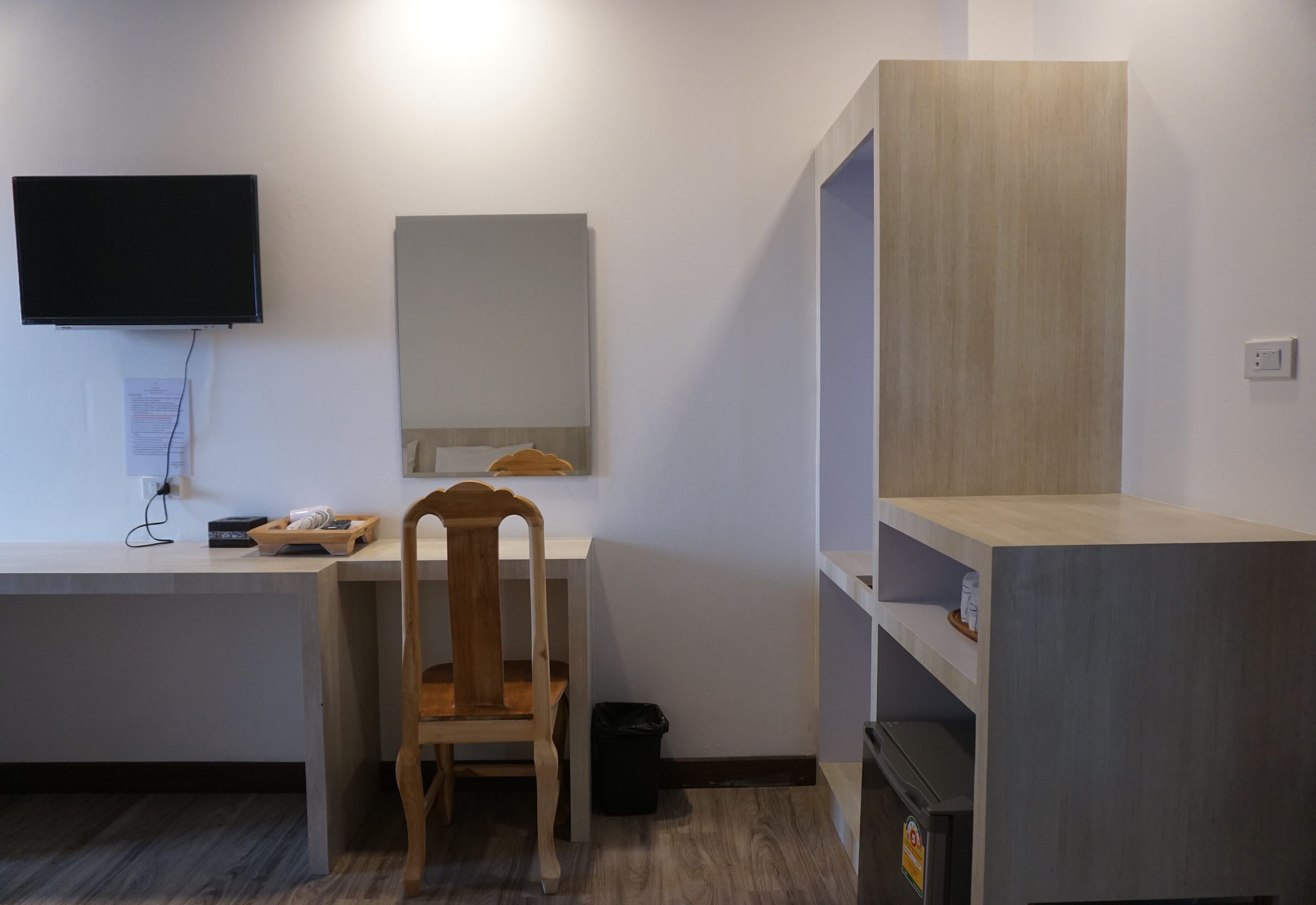 Una habitación con escritorio, silla, televisor, espejo y estanterías empotradas.