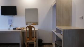 Una habitación con escritorio, silla, televisor, espejo y estanterías empotradas.