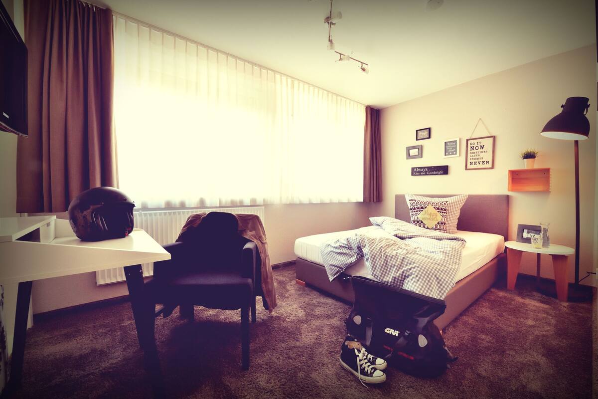 Ein Hotelzimmer mit Bett, Schreibtisch, Stuhl, Heizkörper und einem Vorhangfenster.