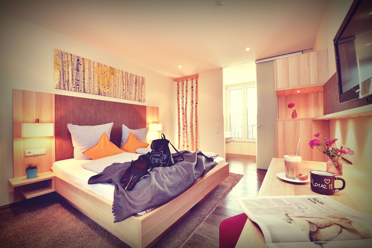 Ein modernes Hotelzimmer mit einem großen Bett, Nachttischen, einem Couchtisch, einem Fernseher und einem Fenster mit Vorhängen.