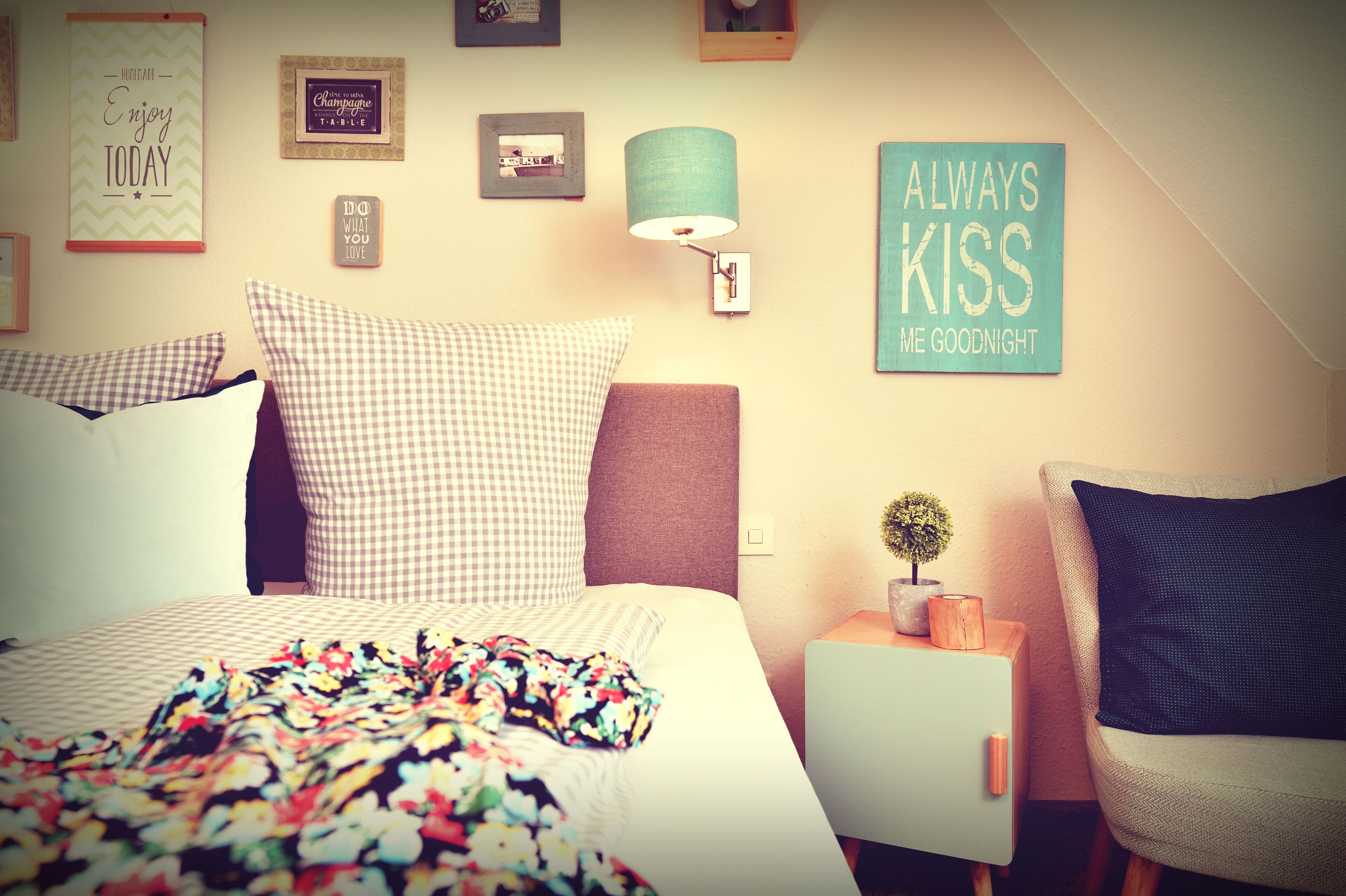 A bedroom with a bed, a nightstand, a lamp, and various wall decorations.