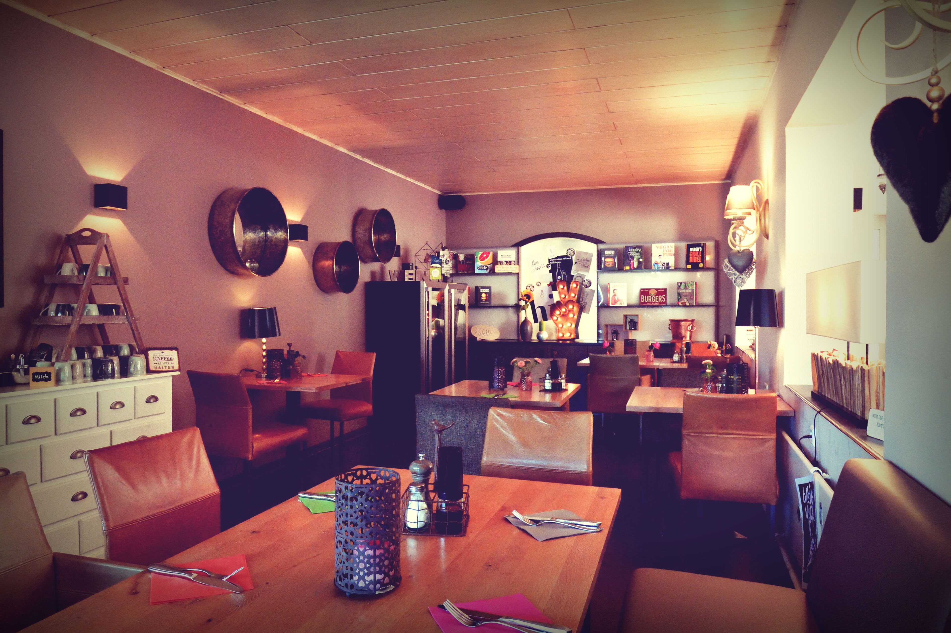 A cozy restaurant with wooden furniture, a bar area, and a kitchen visible in the background.