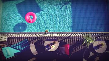 Una piscina en la azotea con un flotador con forma de flamenco rosa, sillas de descanso y vistas de un edificio.