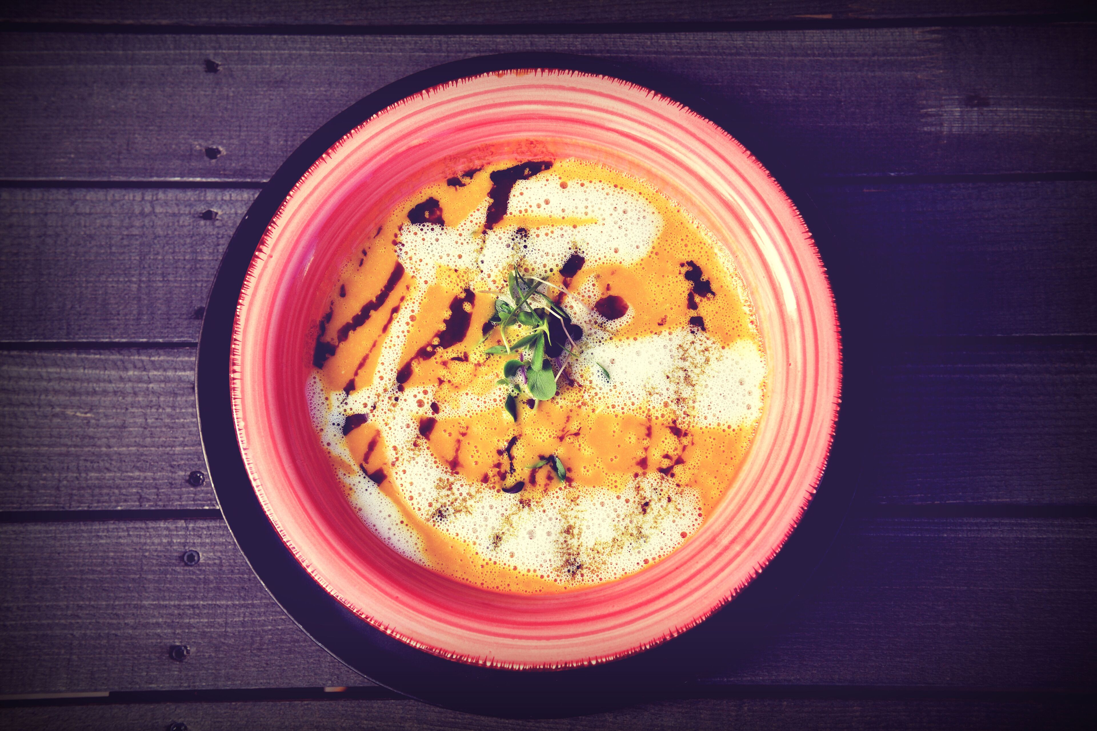 Eine Schüssel Suppe mit rotem Rand auf einem Holztisch.