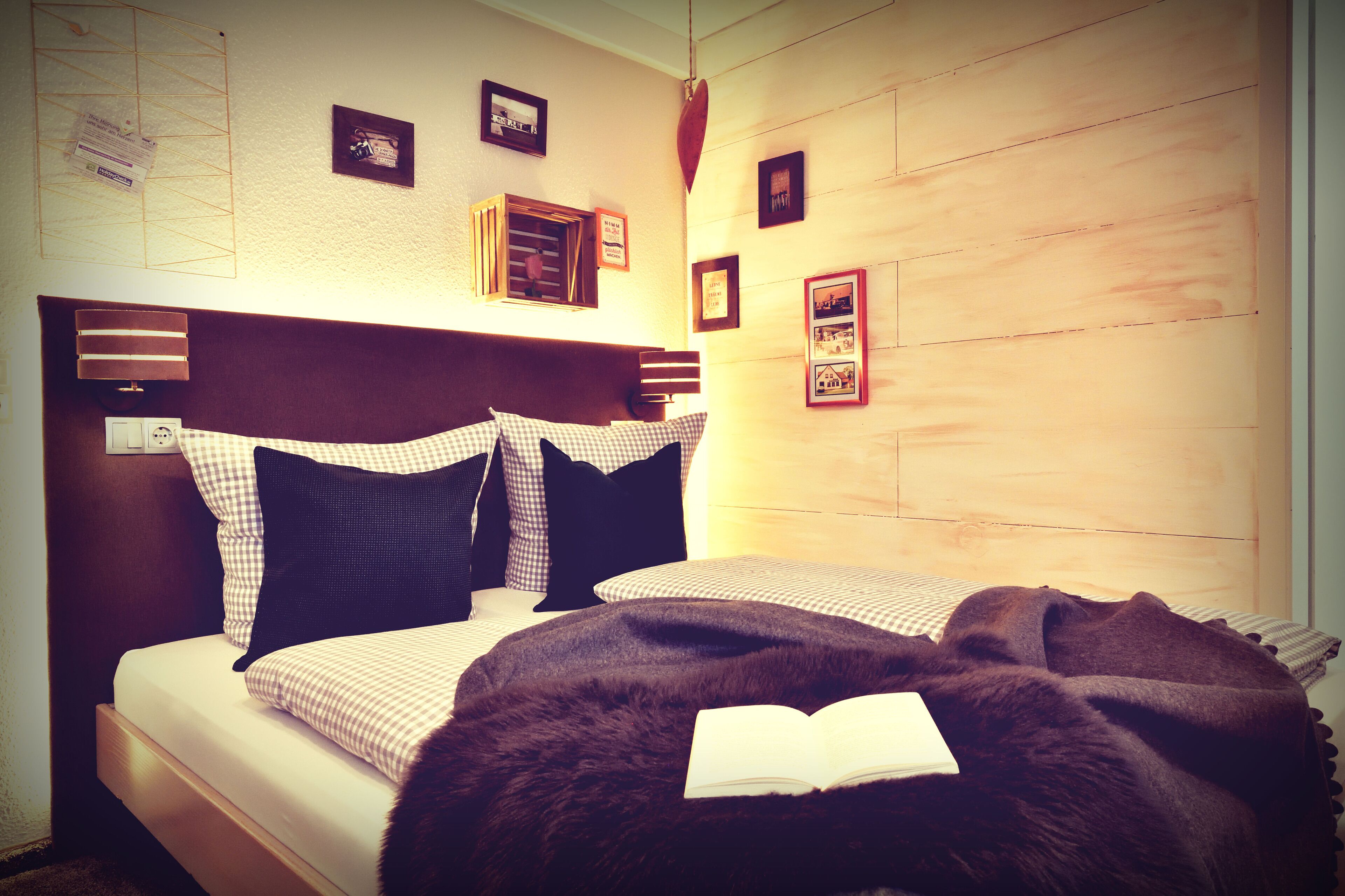 A neatly made bed with a checkered duvet, a dark brown throw blanket, and an open book on the pillow.