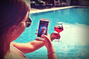 A person holding a smartphone and a glass of red drink by a pool. - Melbo’s Home (Lindau)