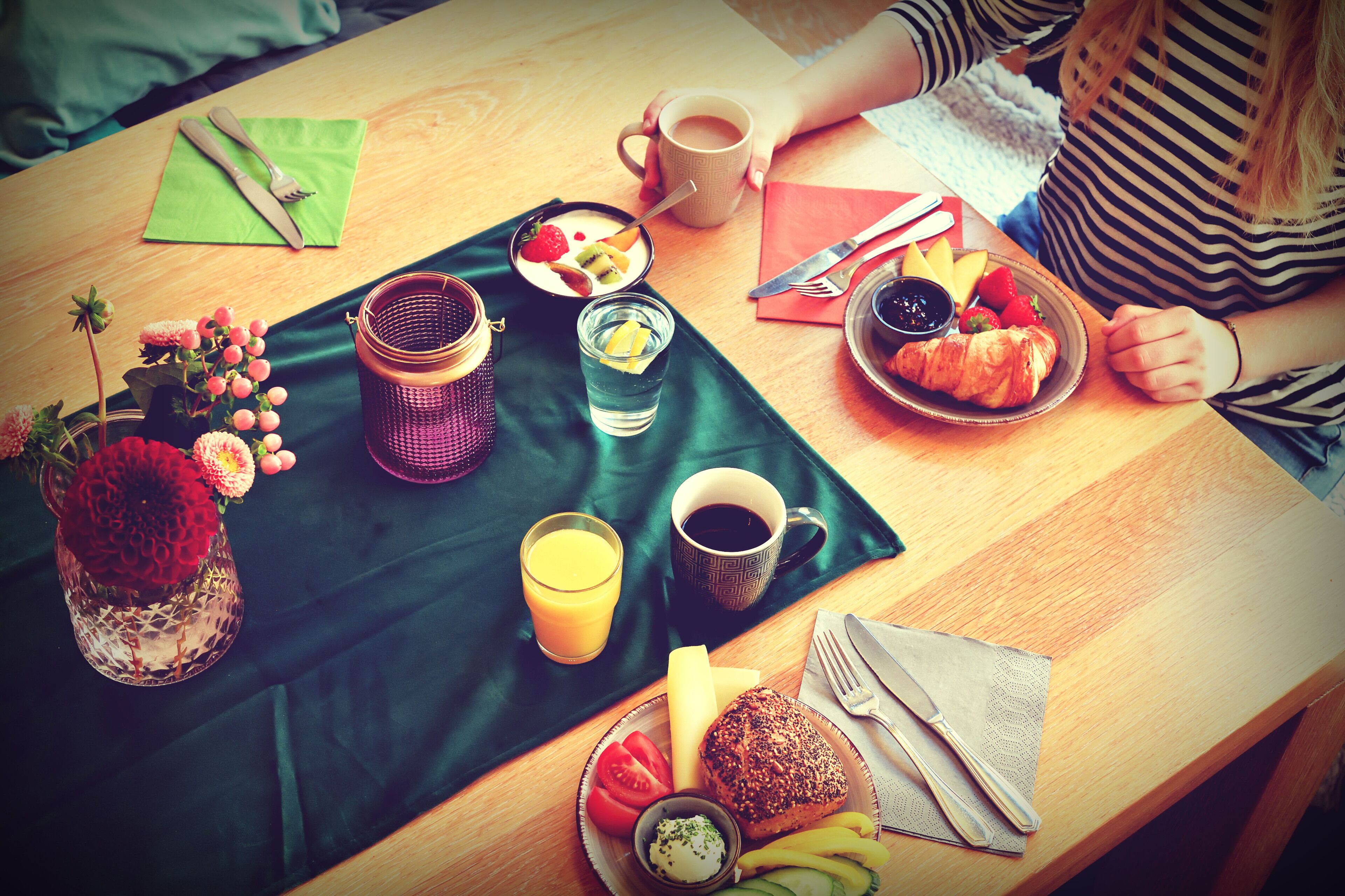 Une table de petit-déjeuner avec divers aliments, une tasse de café et un vase de fleurs.
