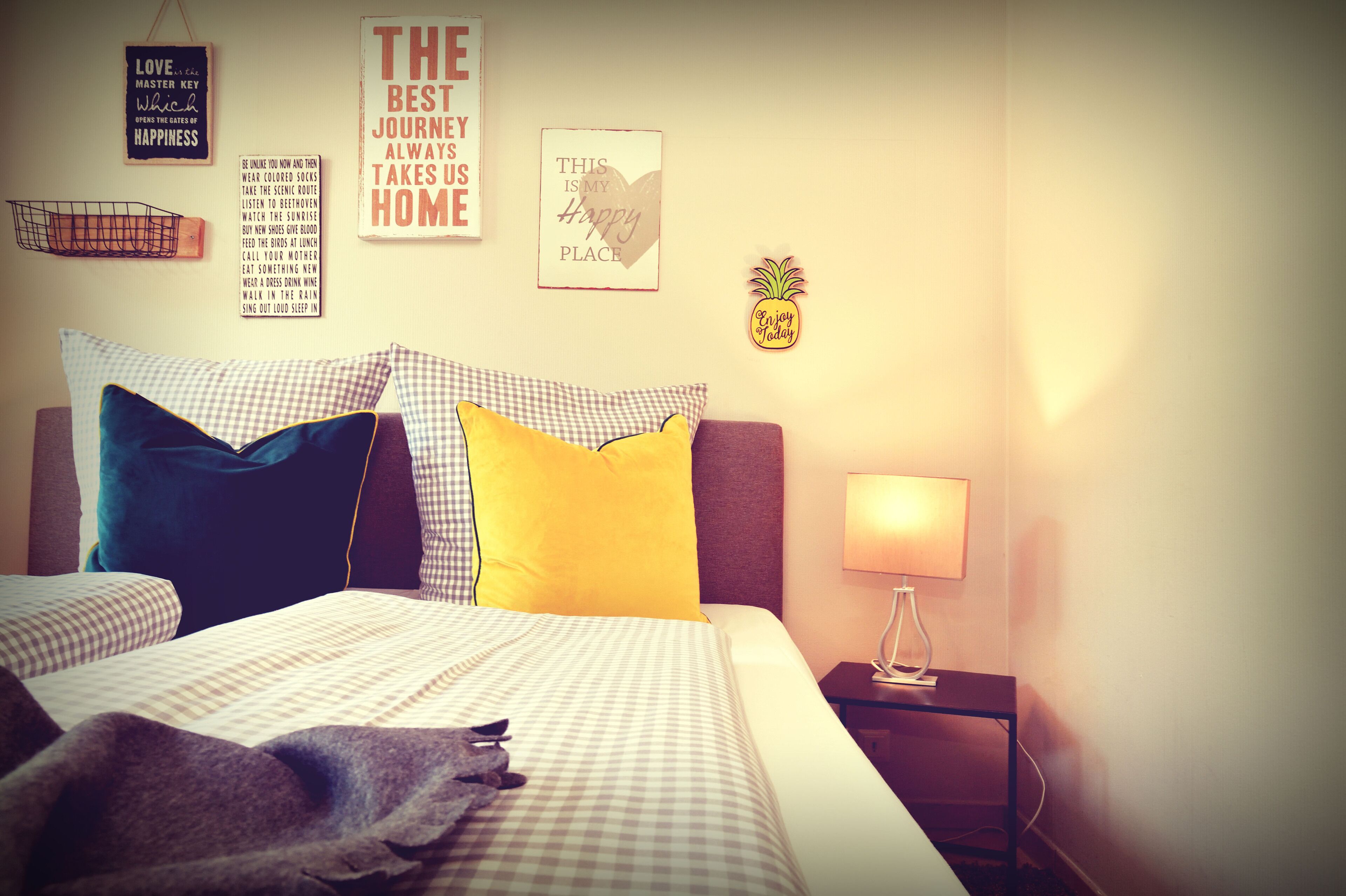 A neatly made bed with checkered bedding, a lamp on a bedside table, and motivational wall art.
