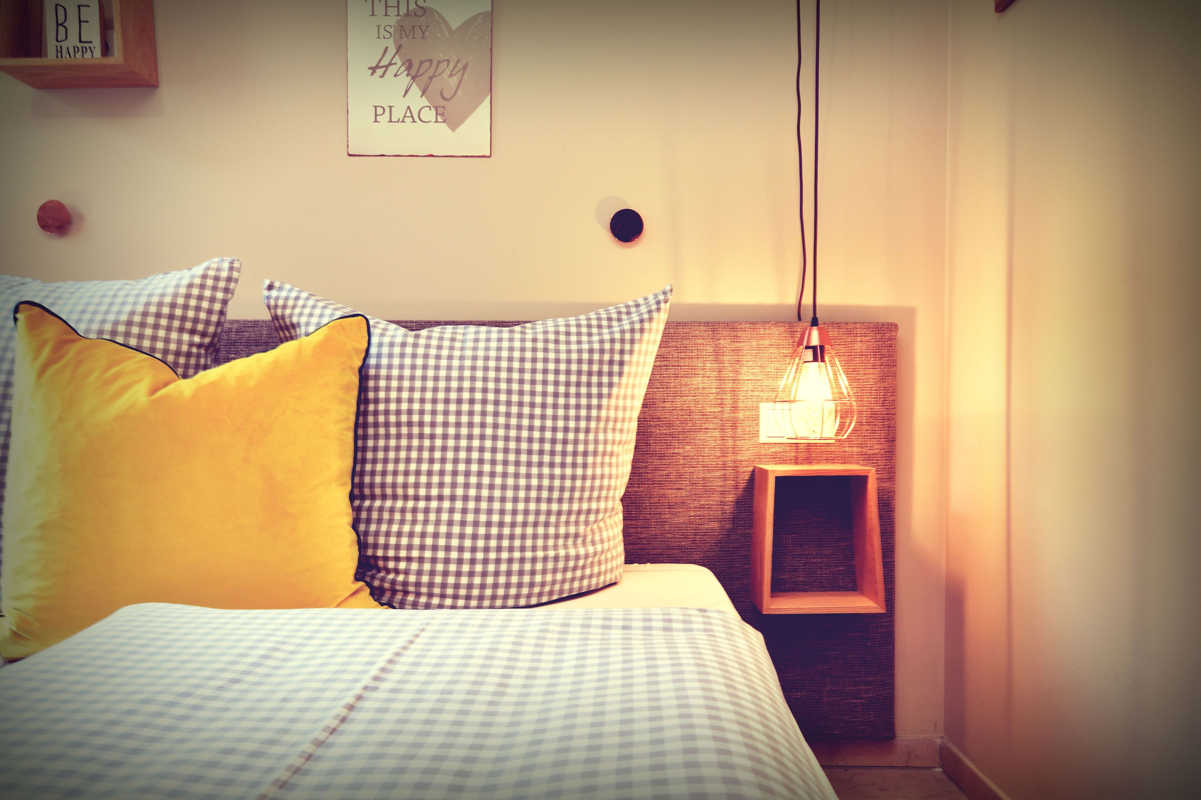 Un lit avec une couette à carreaux, un oreiller jaune et un luminaire fixé au mur.