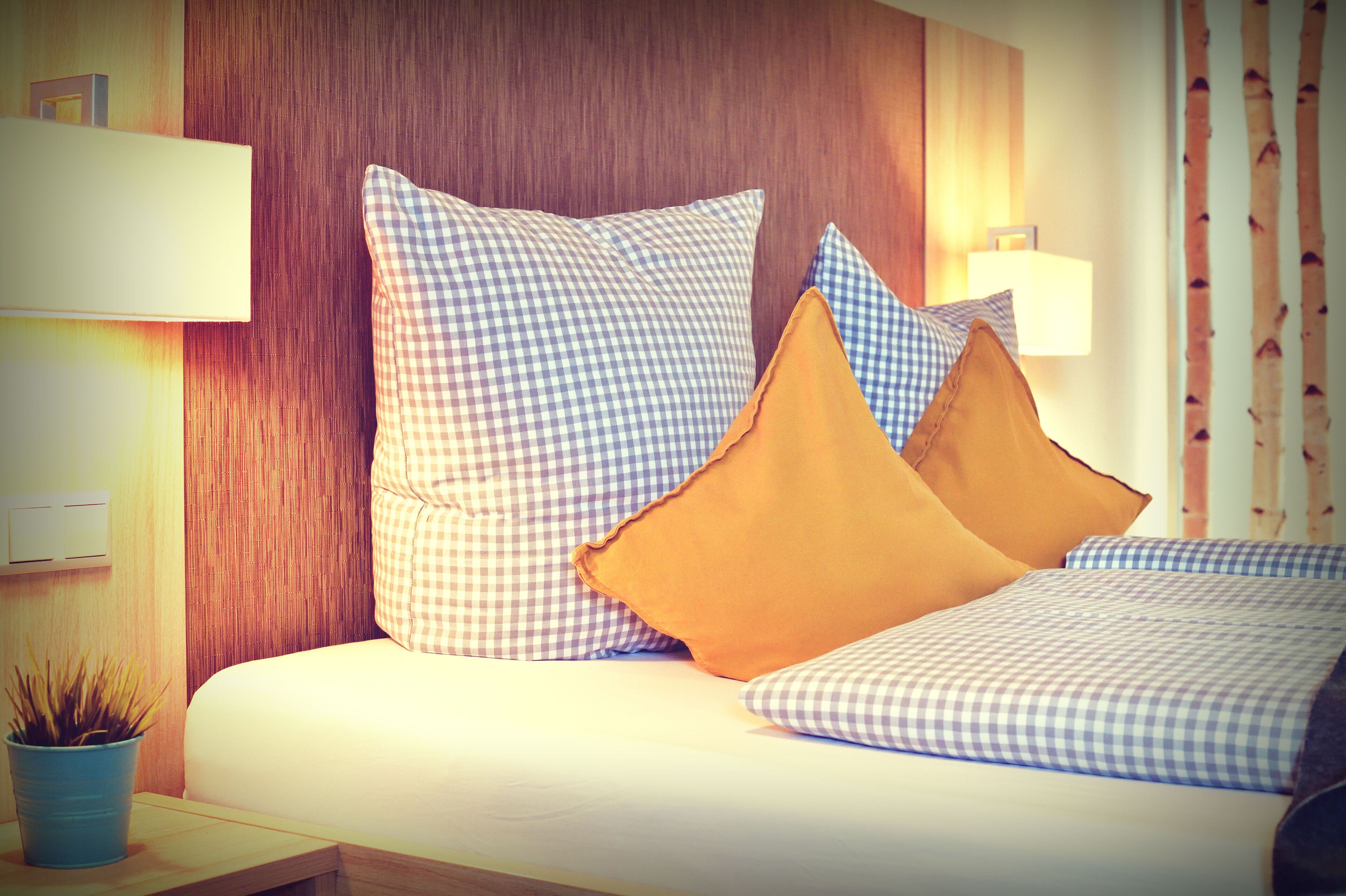 Una cama con ropa de cama a cuadros, un cabecero de madera y una lámpara de noche.