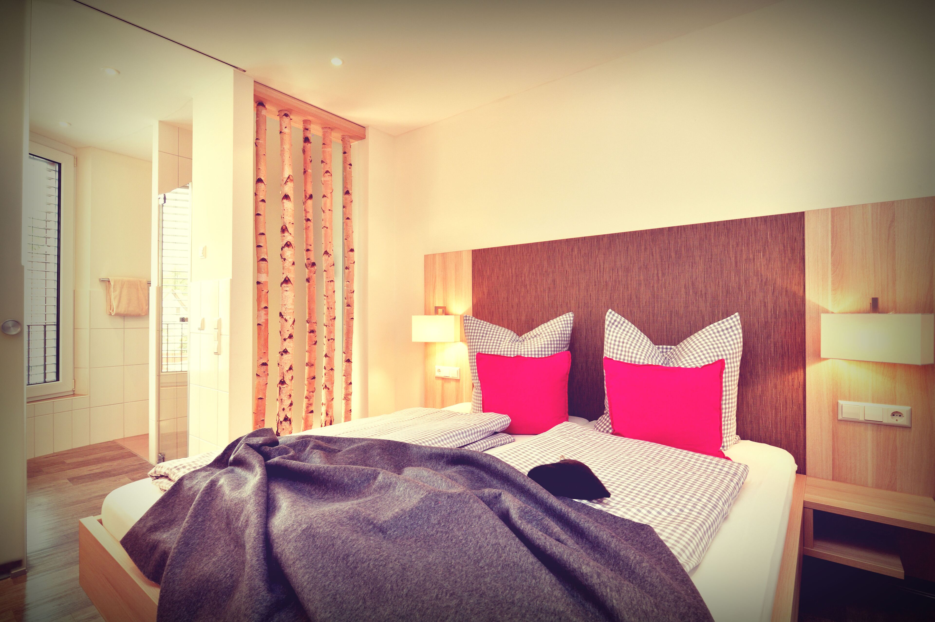 A hotel room with a bed, a wooden headboard, a nightstand, and a window with curtains.