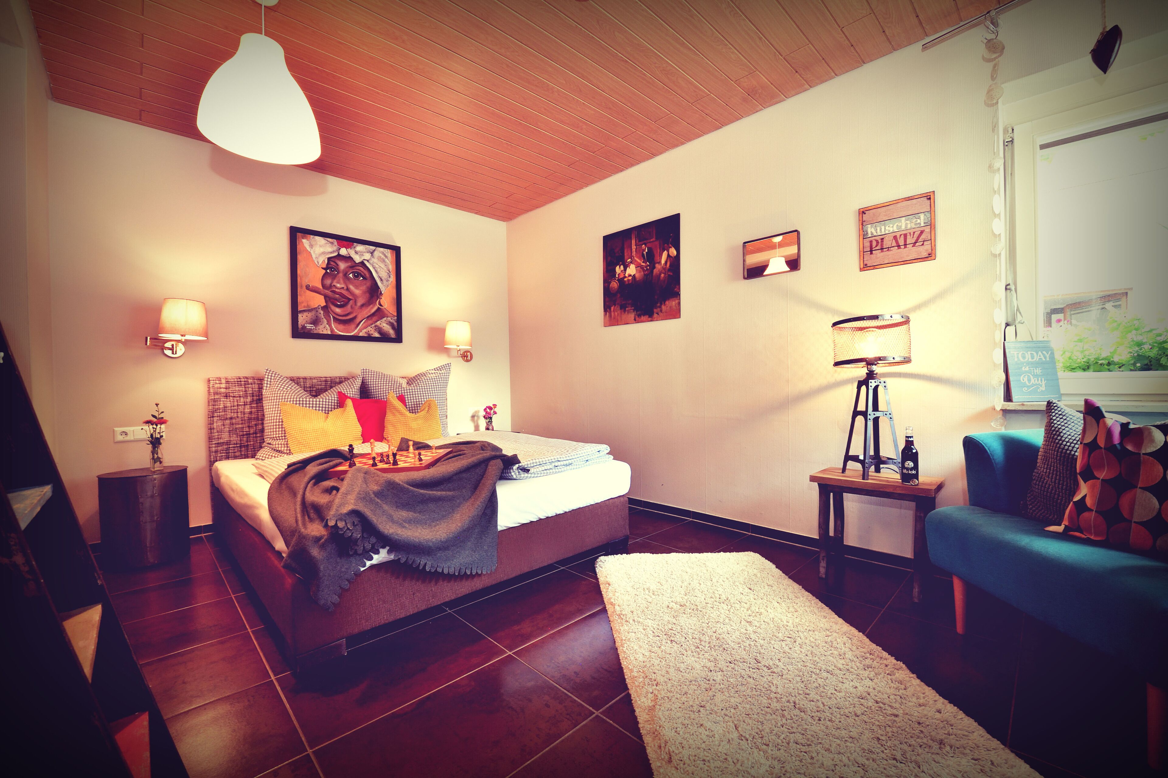 Un dormitorio con cama, mesitas de noche, lámpara, sofá y decoración en la pared.