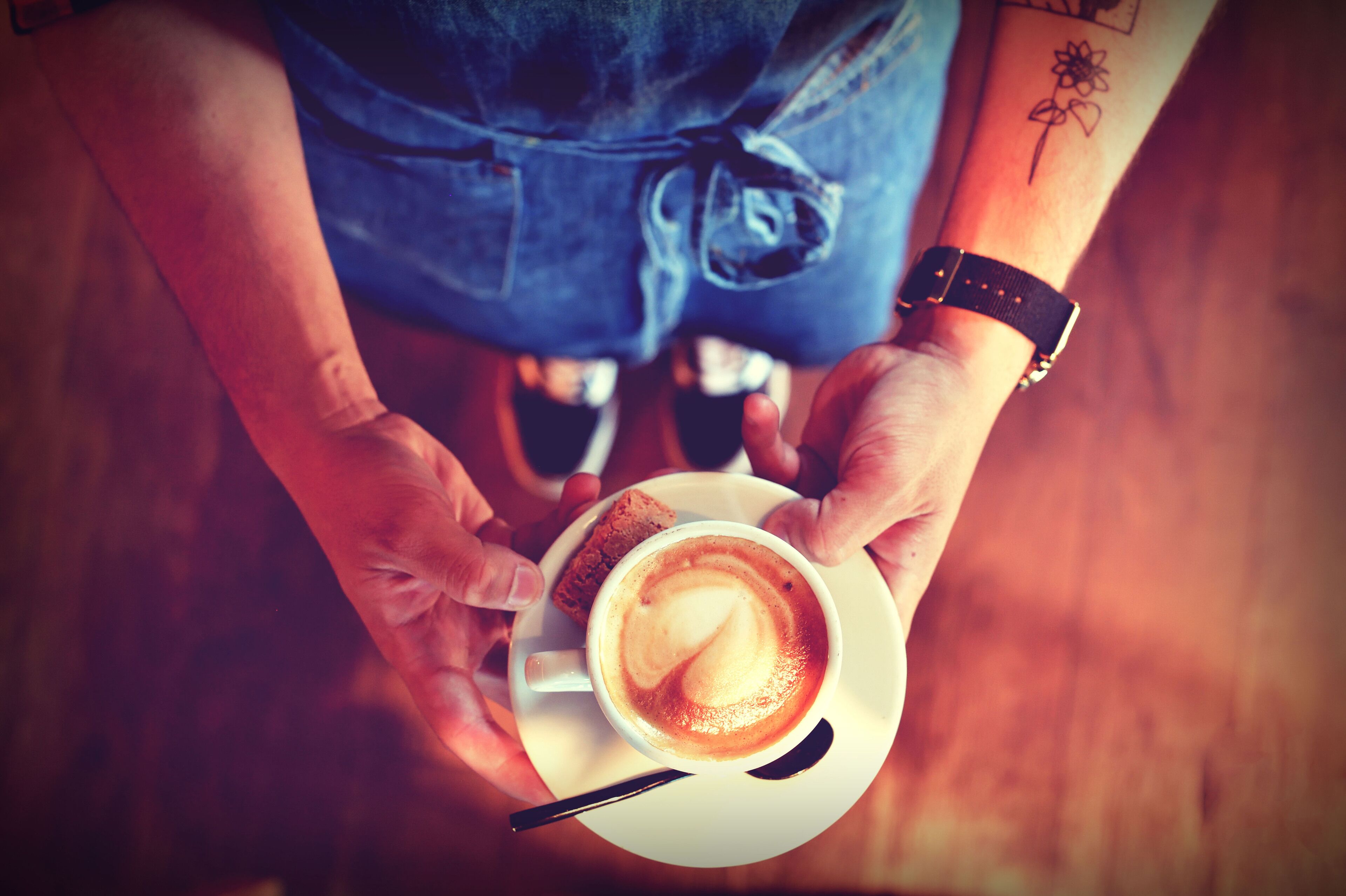 A person holding a cup of coffee with a saucer and a spoon.