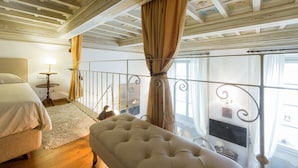 Un dormitorio con cama, un sillón, una mesita de noche con lámpara y vistas al exterior a través de una ventana con cortinas.