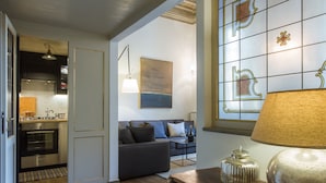 Una sala de estar moderna con un sofá, una mesa de centro y una lámpara. Se ve una cocina al fondo.