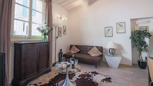 A living room with a wooden cabinet, a glass coffee table with decorative items, a brown leather sofa, a glass side table with a lamp, and a cowhide rug. - Pandolfini Roof (Florence)