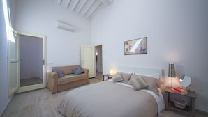 A bedroom with a bed, a sofa, a bedside table with a lamp, a mirror, and a picture on the wall. - Pandolfini Roof (Florence)