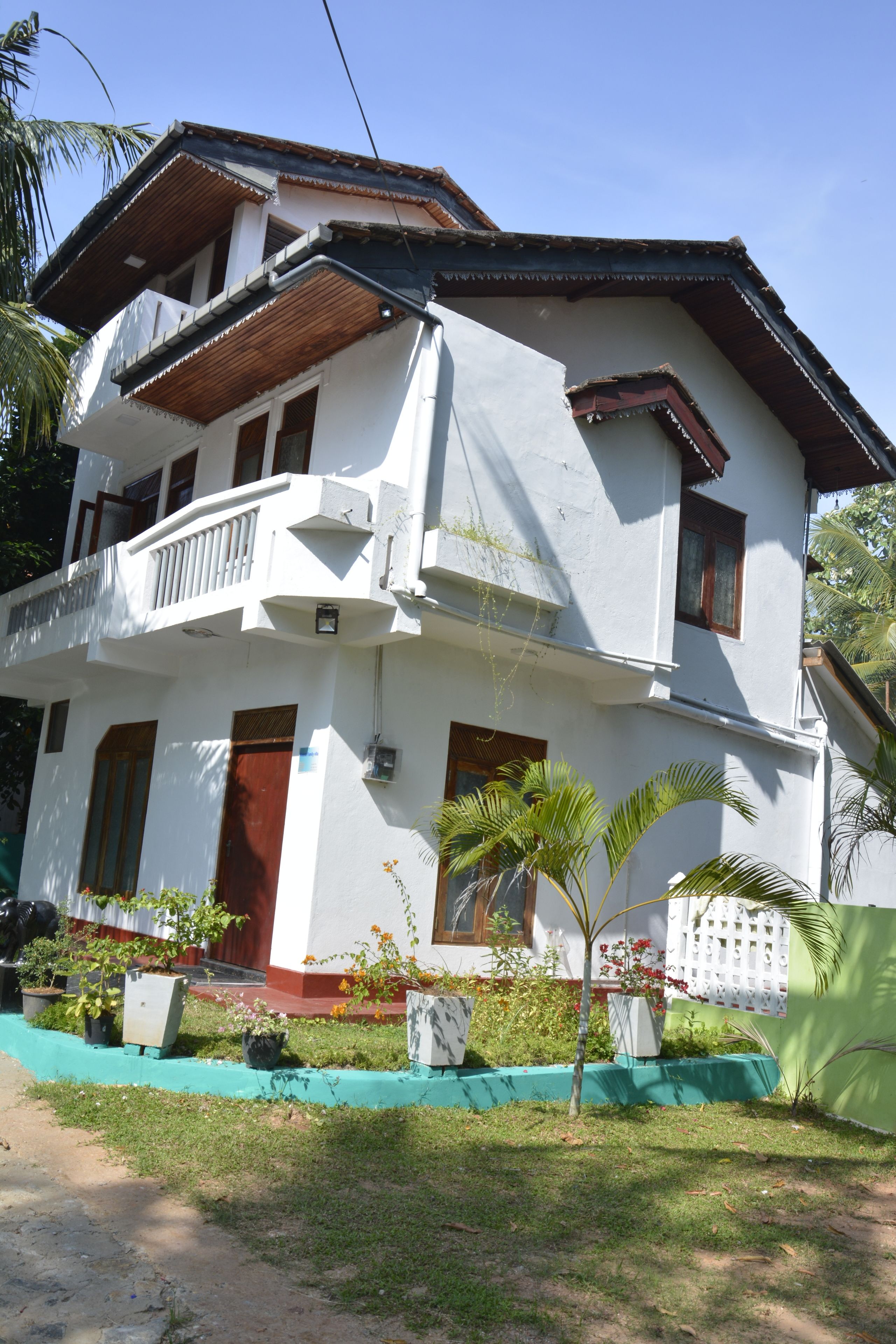 A two-story house with a balcony, a red door, and a green lawn.