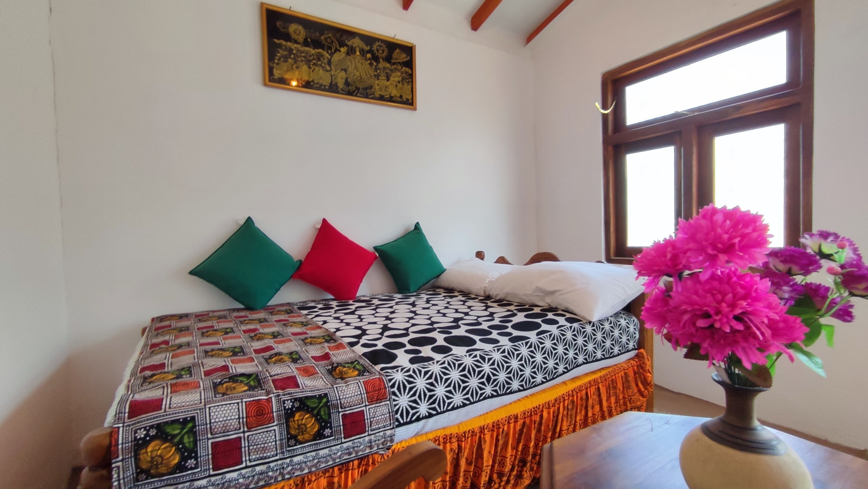 A bed with patterned bedding, pillows, and a vase with flowers.