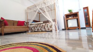 A room with a wooden sofa, a colorful striped rug, a canopy bed, and a small wooden cabinet with a plant. - Matota Family Villa (Matara)