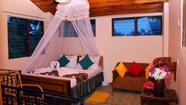 A bedroom with a canopy bed, a wooden ceiling, a sofa with colorful cushions, and a vase of flowers. - Matota Family Villa (Matara)