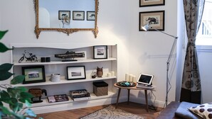A living room with a white fireplace, a large ornate mirror, framed pictures on the wall, a laptop on a side table, and a potted plant. - Pandolfini Suite (Florence)