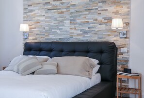 A modern bedroom with a stone-patterned wall, a black upholstered headboard, and two bedside lamps.