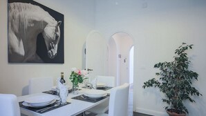A dining area with a white table set for two, a potted plant, and a large painting of a horse. - Pandolfini Suite (Florence)